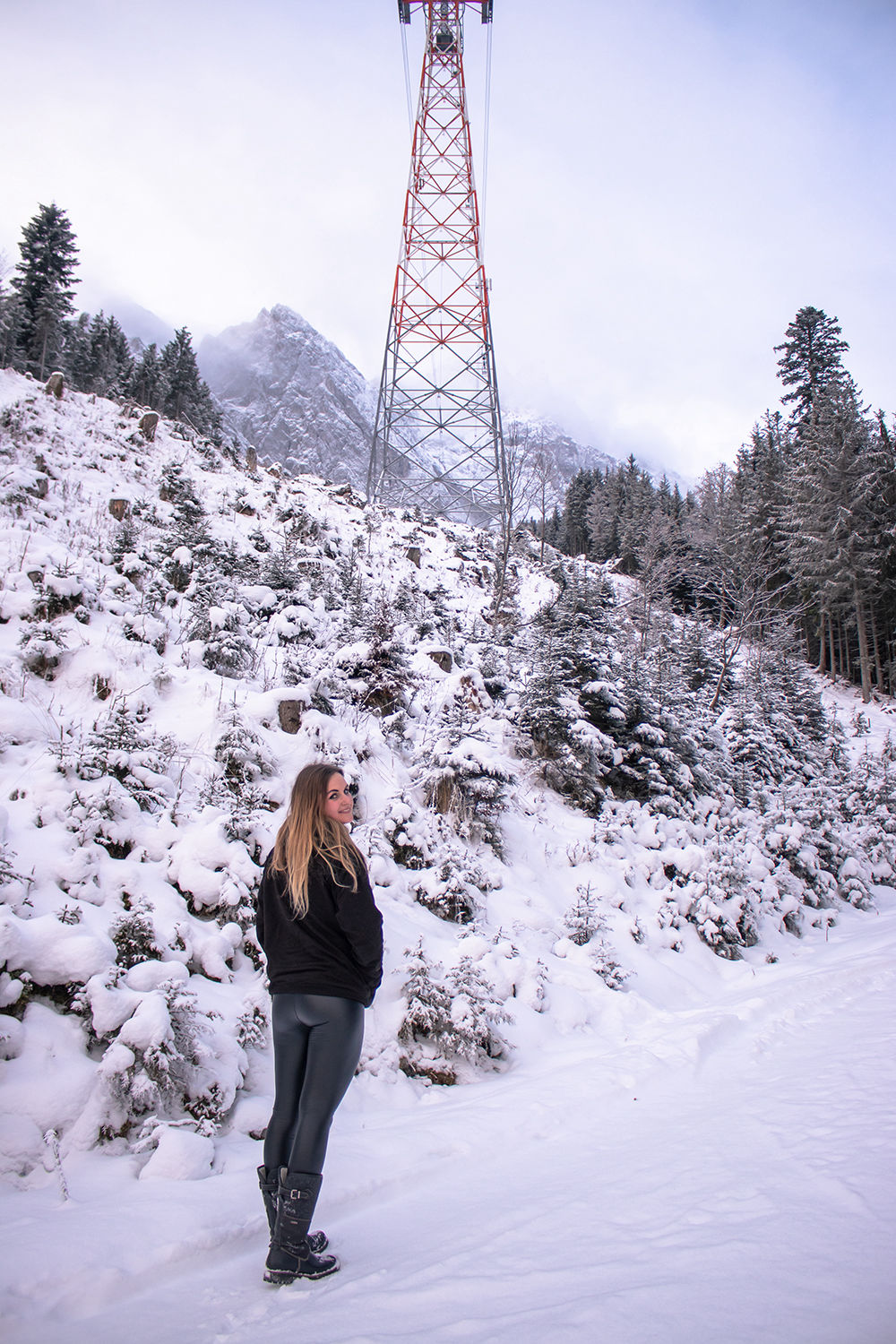 Eine Frau steht in der Landschaft von Alpen und Schnee und gegenüber Freileitungsmast
