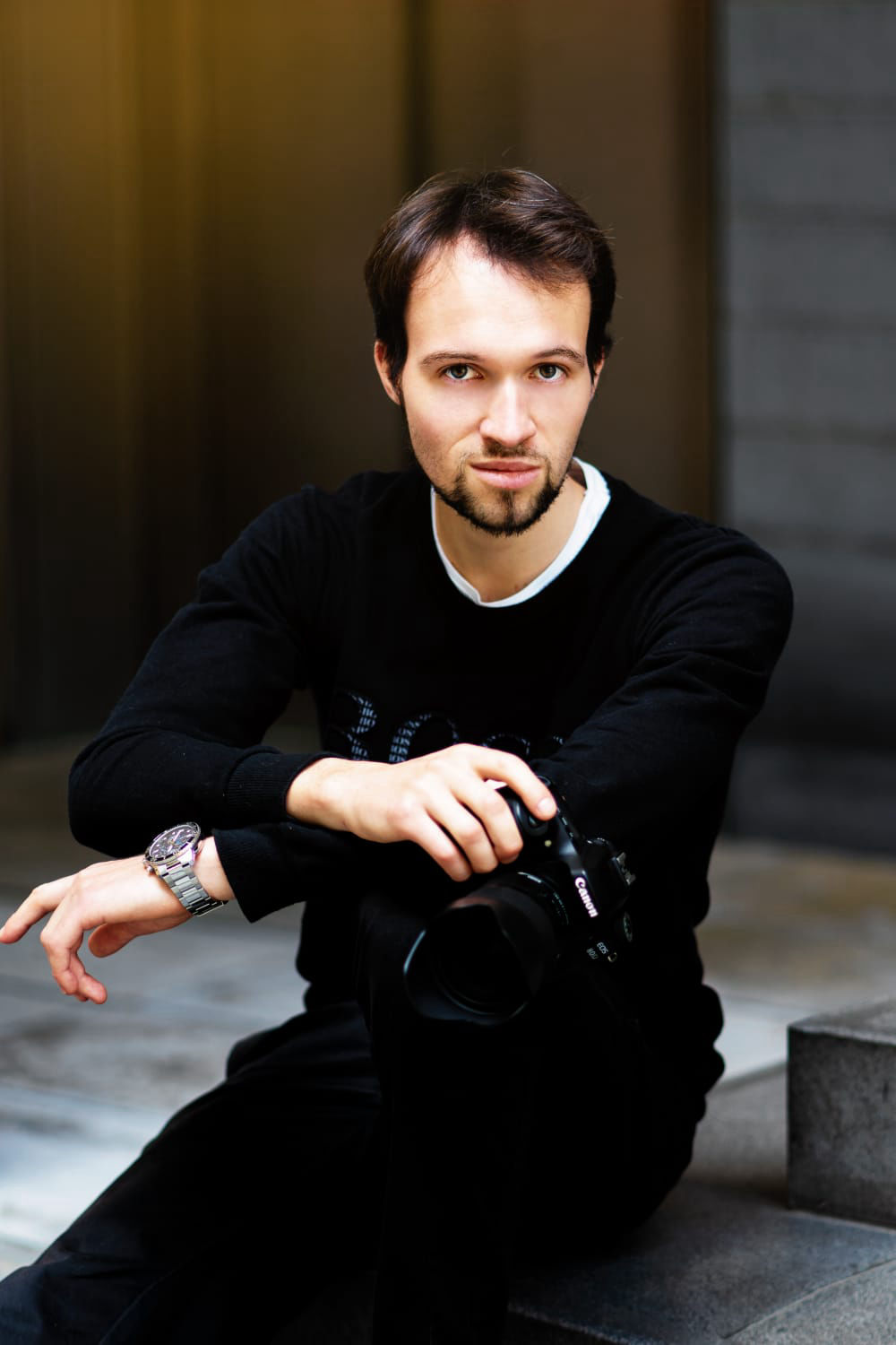 Junger bärtiger Mann und Fotograf sitzt auf Stufen mit einer Kamera Canon 80d und einer Tissot Luxusuhr